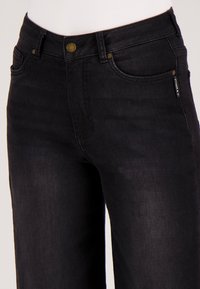 Close-up van de taille en bovenbeen van zwarte denim jeans met een koperen knoop en gestikte zakken op een witte achtergrond.