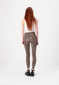 Leopárdmintás leggings, rugalmas anyagból, magas derekú kivitel, testhezálló fazon, fekete cipővel párosítva, hátulról látva.