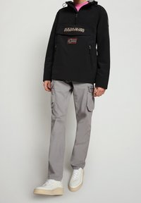 Schwarze Kapuzenjacke mit einer Vorder- tasche, Logoaufnäher und Norwegen-Flaggen-Detail. Kombiniert mit hellgrauen Cargo-Hosen und weißen Sneakers.