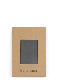 Bruine kartonnen verpakking met een transparant gaasvenster waarin zwart materiaal zichtbaar is; "SUITABLE" logo in donkere letters gedrukt aan de onderkant.