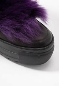Černé platformové tenisky s texturovanou gumovou podrážkou. Horní část pokrývá fialový umělý kožíšek, což poskytuje kontrastní měkkou texturu.