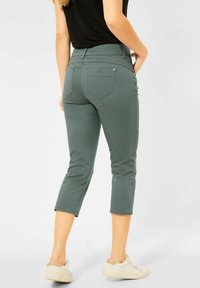 Gröna cropped byxor i mjuk bomullsblandning, med midjehöjd i mitten, bakfickor och uppvikta benslut. Matchat med vita skor.