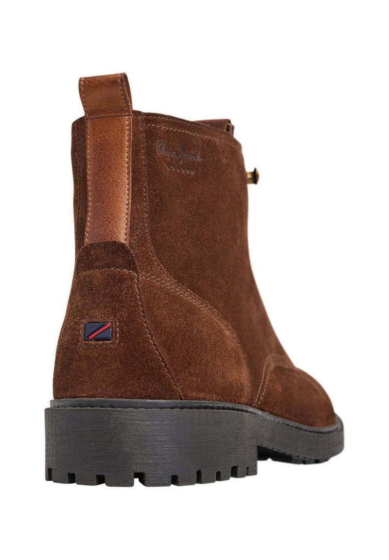 Botín de ante marrón con un acento de cuero marrón, que presenta un talón reforzado, suela de goma negra texturizada y un pequeño detalle de logotipo.