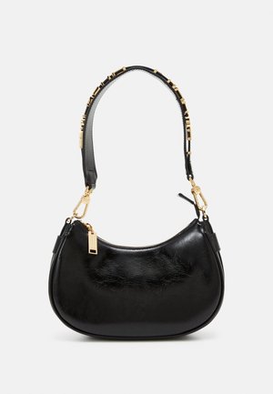 Schwarze, halbmondförmige Lederhandtasche mit goldenem Reißverschluss und dekorativer goldener Beschlag am kurzen Schulterriemen vor einfachem Hintergrund.
