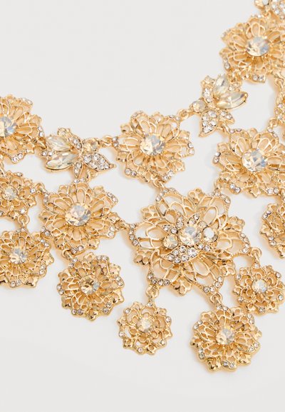 Ogrlica z zlatim tonom z cvetličnim vzorcem, prozornimi bleščicami in zapletenimi filigranskimi detajli na belem ozadju.