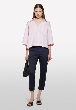 Chemise courte rose clair avec un col, fermeture à boutons et une poche poitrine, associée à un pantalon navy fuselé, un sac tissé noir et des sandales noires.