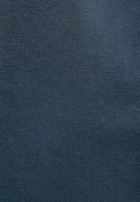 Tessuto di denim blu scuro con una sottile texture a coste, che mostra schemi di tessitura diagonale e una finitura superficiale liscia.