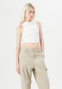 Vit ribbad ärmlös crop top som bärs med beiga cargo-byxor med fickor på sidan och en avslappnad passform.