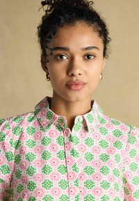 Lillelillelise mustriga särk, millel on roosa ja roheline disain, laia kraega ja nööpidega kinnitamine. Valmistatud kergest kangast, millel on sile tekstuur.