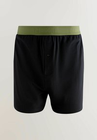 Melnas bokseršortus, kas izgatavoti no mīksta materiāla, ar vienkāršu zaļu elastīgu jostu, kas ir ar tekstūrētu virsmu un vienu pogu priekšā.