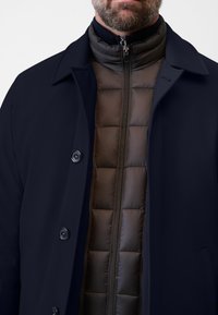 Marinblå kapp med en slät yta, som har svart vaddering under. Framställning med dragkedja och synliga detaljknappar.