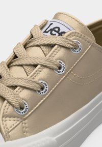 Μπεζ αθλητικό παπούτσι με κορδόνια με παχύ υφή, λευκή σόλα και μεταλλικά πατήματα με τη σήμανση "Lee 1889".