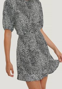 Vestido de lunares en blanco y negro con mangas cortas abullonadas, cintura fruncida y dobladillo con volantes, hecho de tela ligera.