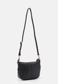 Sac à épaule en cuir noir avec une texture lisse, doté d'une fermeture éclair, d'une sangle réglable et d'accents en métal doré.