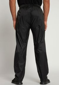 Zwarte, lichte, waterafstotende broek met een elastische tailleband. Heeft een losse pasvorm en een gladde, glanzende textuur.