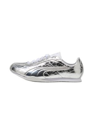 Błyszczący srebrny niski sneaker z białą podeszwą i sznurówkami, z zakrzywionym wzorem pasków po bokach, widoczny od zewnętrznej strony.