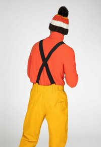 Een oranje coltrui, gele waterdichte broek met verstelbare zwarte bretels, en een kleurrijke gebreide beanie met een pompon detail.
