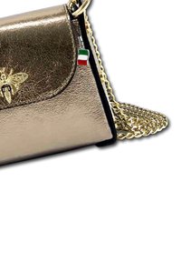 Metallic gold handbag with a flap closure, chain strap, decorative bee emblem, and an Italian flag charm attached. Textured surface.