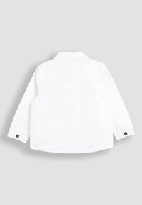 Camicia bianca a maniche lunghe in cotone con taglio dritto, dotata di colletto e dettagli con bottoni marroni sulle maniche.