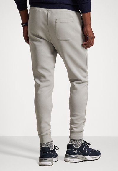 Svetlošedé tepláky vyrobené z jemného materiálu, s zadnou vreckom, úzkym strihom a pružnými nohavicami, doplnené tmavými teniskami.