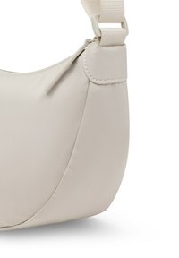 Bolso de hombro en forma de media luna de color beige claro con cremallera y correa de tela ajustable sujeta por un lazo cosido.