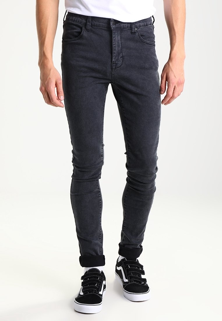 Jeans skinny negros con una textura de denim suave, detalles de costura y un diseño clásico de cinco bolsillos, combinados con zapatillas negras y blancas.
