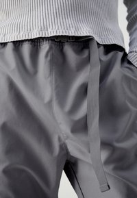 Grå lätta byxor med en slät textur och elastisk midja. Har en platt dragsko och en avslappnad passform. Ribbat grått linne synligt ovanför.