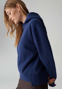 Marineblauer Kapuzenpullover mit lockerem Schnitt, Rippbündchen an Ärmeln und Saum. Weiche Stoffstruktur, mit Kängurutasche und großzügiger Kapuze.