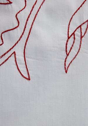 Witte stof met rode geborduurde details, die loofvormen weergeeft met verschillende steekpatronen en een textuurafwerking.