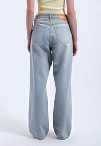 Jean large bleu clair à taille haute, avec une étiquette brune au dos et deux poches arrière. Jambes fuselées et texture en denim.