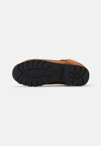Botte en cuir marron avec une surface texturée, semelle en caoutchouc noir dotée d'un motif à crampons et d'un logo de la marque. Détail de fermeture éclair sur le côté visible.