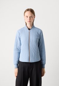 Giacca imbottita di colore blu chiaro con colletto rialzato, chiusura a zip e polsini a coste con strisce a contrasto. Texture liscia e vestibilità sartoriale.
