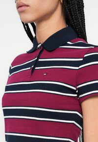 Červené a námornícky modré pruhované polokošeľa s námornícky modrým golierom, vybavená tromi gombíkmi a malým logom značky na hrudi.