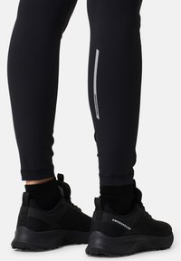 Black athletic leggings made of stretchy material with a slim fit, featuring a reflective stripe. Pair of black running shoes with mesh detail.