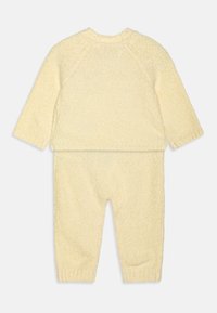 Ensemble en tricot jaune comprenant un haut à manches longues et un pantalon assorti avec des poignets côtelés et une finition douce et texturée.