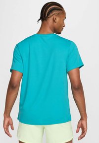 Camiseta de manga corta turquesa hecha de una tela suave, con un cuello redondo clásico y un corte relajado, mostrada desde la parte de atrás.