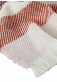 Gelaagd geweven deken in zachte tinten van roze en rood. Heeft afwisselende strepen en franjes aan de randen. Gemaakt van warm, comfortabel materiaal.