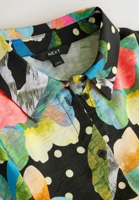 Košile s květinovým vzorem na černém pozadí, zdobená barevnými listy a puntíky. Vyrobena z lehké látky s límečkem.