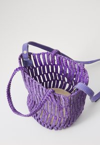 Purple woven tote bag with an open structure, featuring a flat bottom and leather straps. The material shows a textured, braided design.