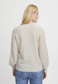Light beige sweater with a soft texture, raglan sleeves, and a ribbed hem. Worn with blue jeans, showing a casual back view.