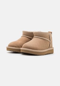 Tan suede ankle boots with a soft fur lining, rounded toe, and a textured rubber sole. Features stitched accents and a low heel.