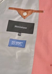 Interno in tessuto grigio con una tasca finta marrone, etichetta nera con la scritta "Matinique" e etichetta blu con la dicitura "Tessuto lavabile".