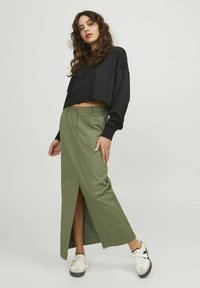 Sudadera negra corta con mangas largas combinada con una falda larga verde oliva con una abertura frontal, usada con zapatillas blancas.