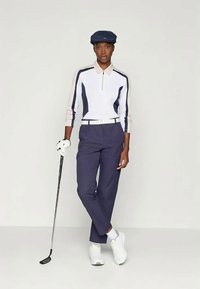 Golf apģērbs, kas sastāv no baltas garām piedurknēm polo krekla ar tumši zilu akcentu, tumši ziliem biksēm, tumši zilu cepuri un baltiem apaviem. Tur rokā golfa nūju.