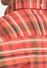 Camicia a quadri rossa con strisce varie in tonalità di rosa, verde e marrone, con collo classico e chiusura a bottoni. Tessuto dalla texture morbida.