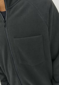 Tmavě šedá fleecová bunda se zipem vpředu, raglánovými rukávy a náprsní kapsou. Měkká textura bez viditelných vzorů či ozdob.