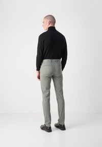 Top negru cu maneci lungi si pantaloni de culoare verde deschis, cu o croiala slim fit, textura neteda si doua buzunare la spate, asortati cu pantofi negri.