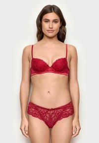 Rød lingerie sæt bestående af en blonde bh med bøjler og justerbare stropper, parret med matchende blonde trusser udsmykket med en sløjfedetalje.