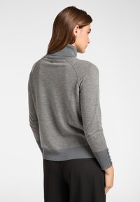 Grauer Pullover mit hohem Kragen, gerippten Bündchen und Saum, versehen mit Knopfdetails an den Bündchen. Weiche, gestrickte Textur mit lässiger Passform.