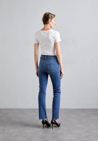 High-waisted blue jeans with a slim fit, featuring back pockets, slight fraying at the hem, worn with a fitted white top and black high heels.